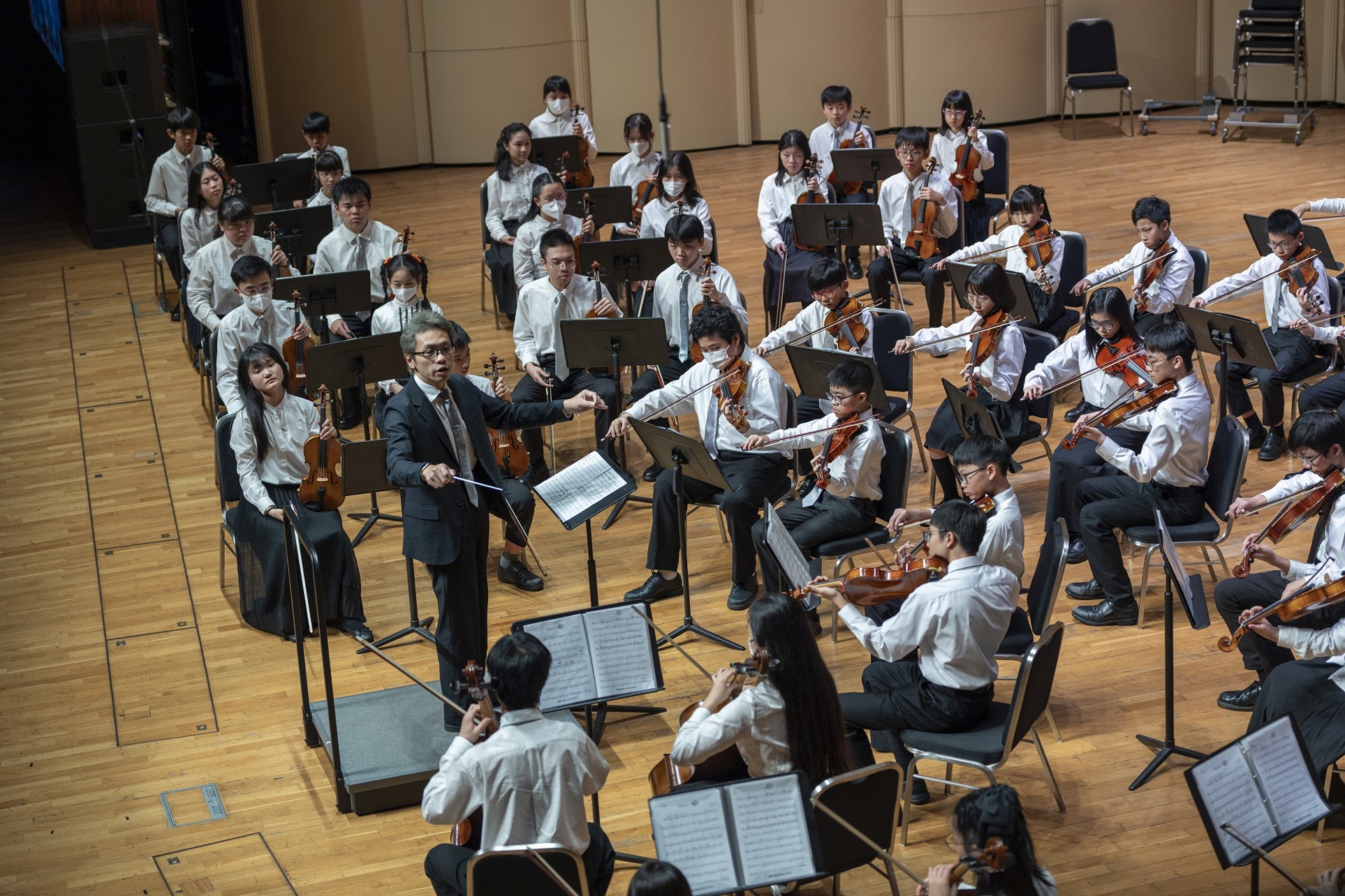 青年管弦樂團在音樂廳演出，指揮帶領弦樂演奏。